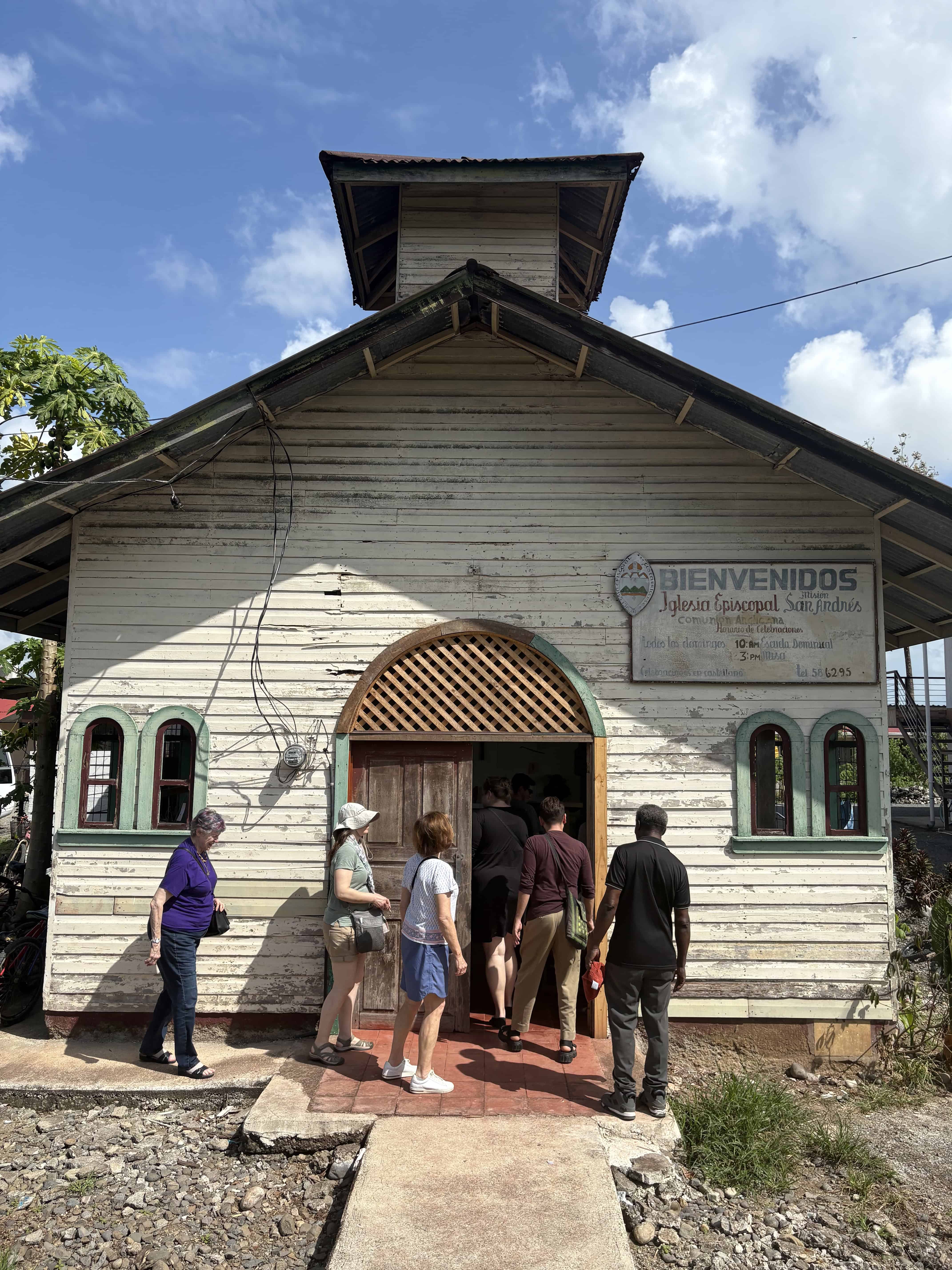 Historic wooden church with visitors entering on a sunny day.
